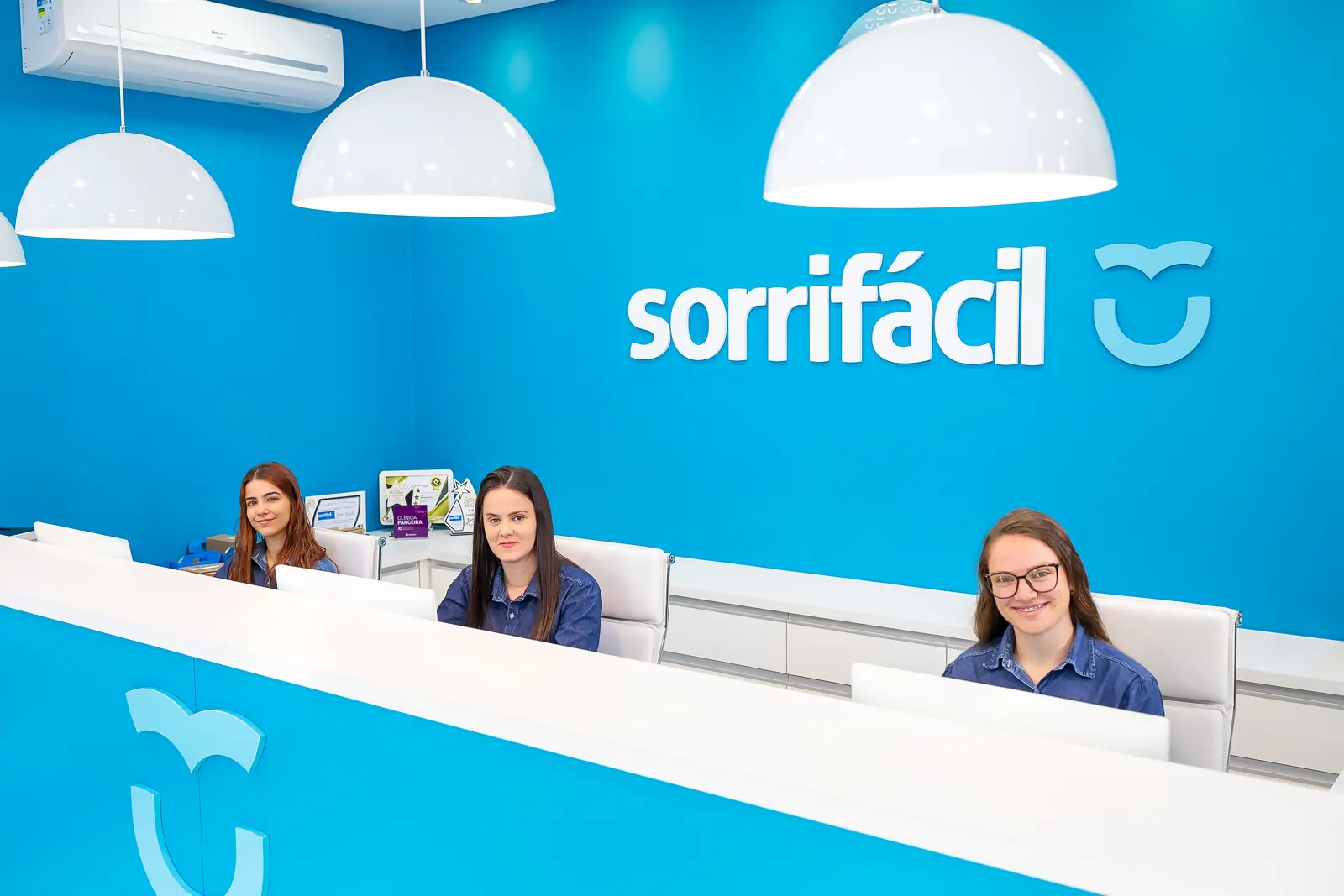 Atendentes na recepção da Sorrifácil Canguçu, em frente ao logo da clínica